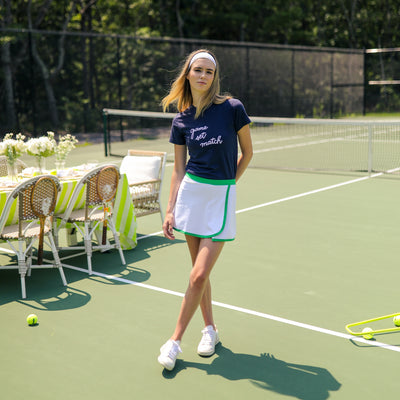 Blonde woman stands on a tennis court wearing a navy tshirt with the words "game set match" embroidered on the front in white
