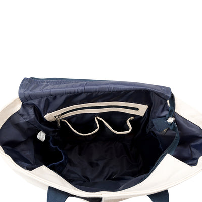 Inside view of natural canvas baseline pickleball tote. Tote has navy trim and handles. Embroidered navy crossed paddles on the front. Front slip pocket is holding a pickleball paddle