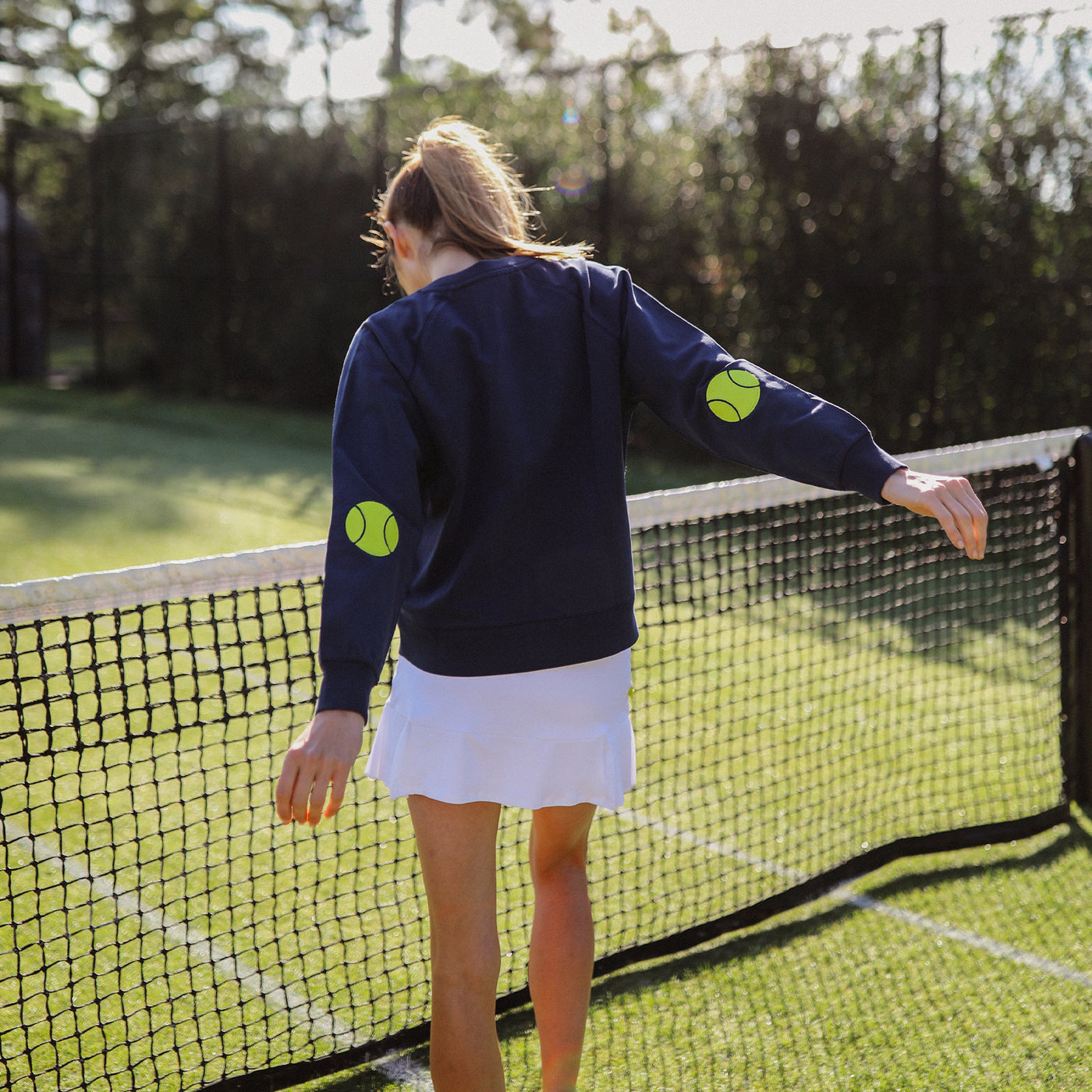 Navy women's sweatshirt with lime embroidery on neckline that reads "tennis anyone" and embroidered tennis ball patches on the elbows.