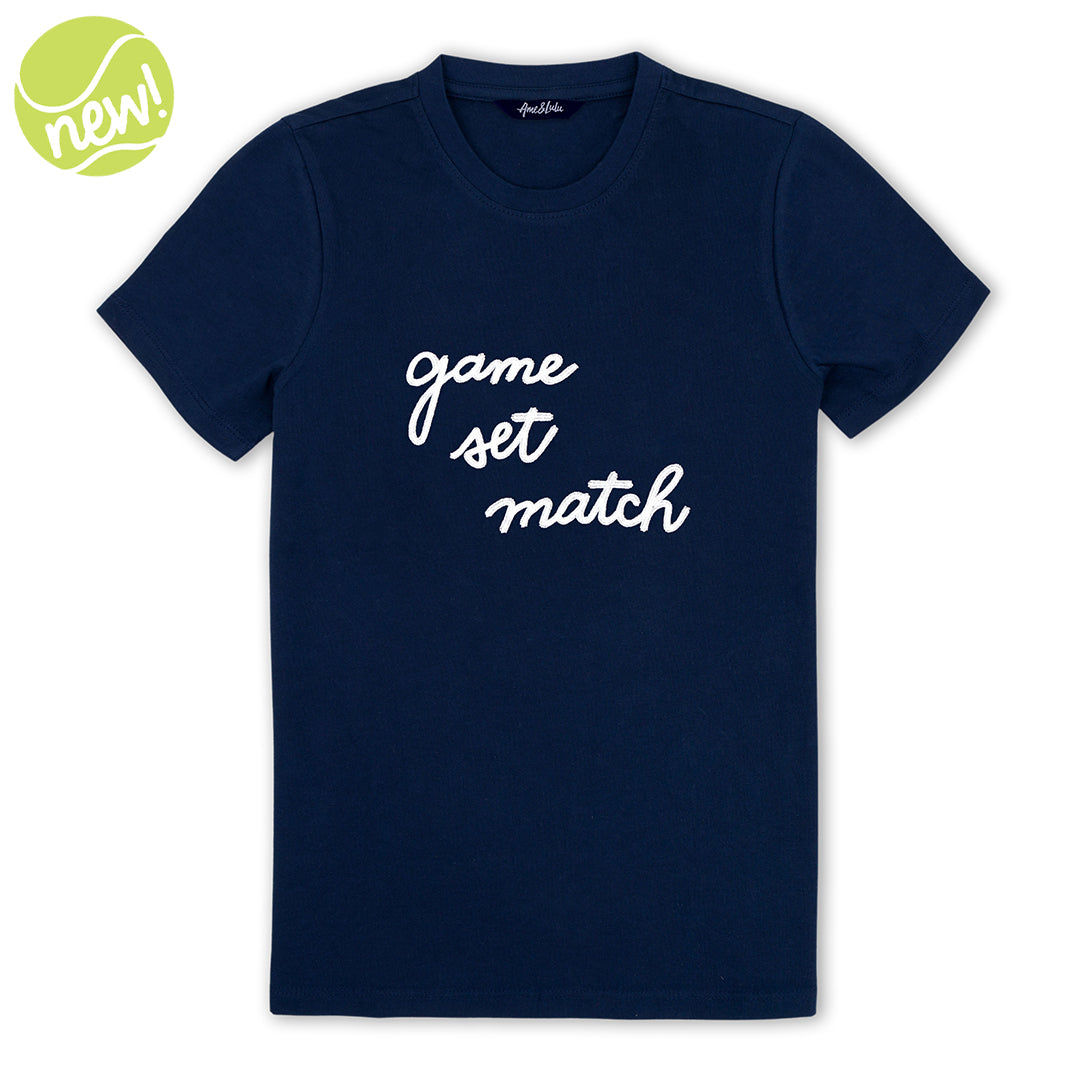 Navy t shirt lays flat on a white background with the words "game set match" embroidered on the front in white