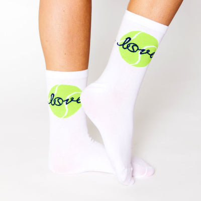 woman wears a pair of white socks with a lime green tennis ball and the word love stitched around the ankle