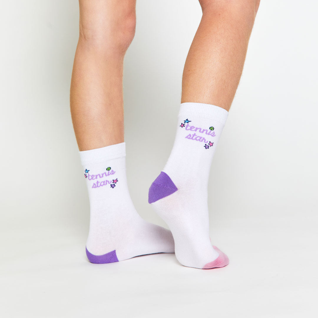 girl wearing pair of white kids crew socks with purple and pink heel and toes. Sides stitched with words tennis star in purple cursive font.