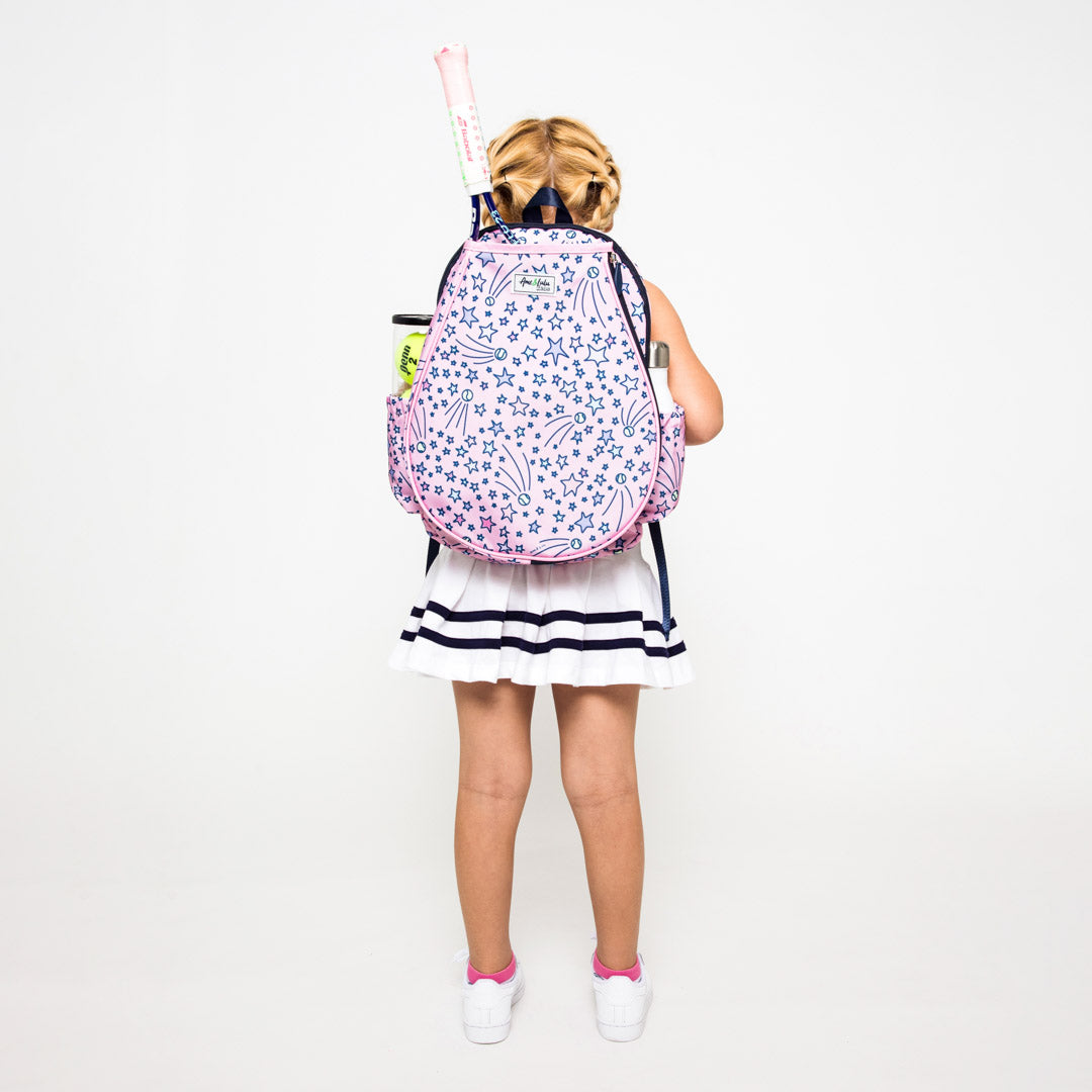 Little girl wearing a light pink kids tennis backpack with pink and purple shooting stars and tennis balls on bag.