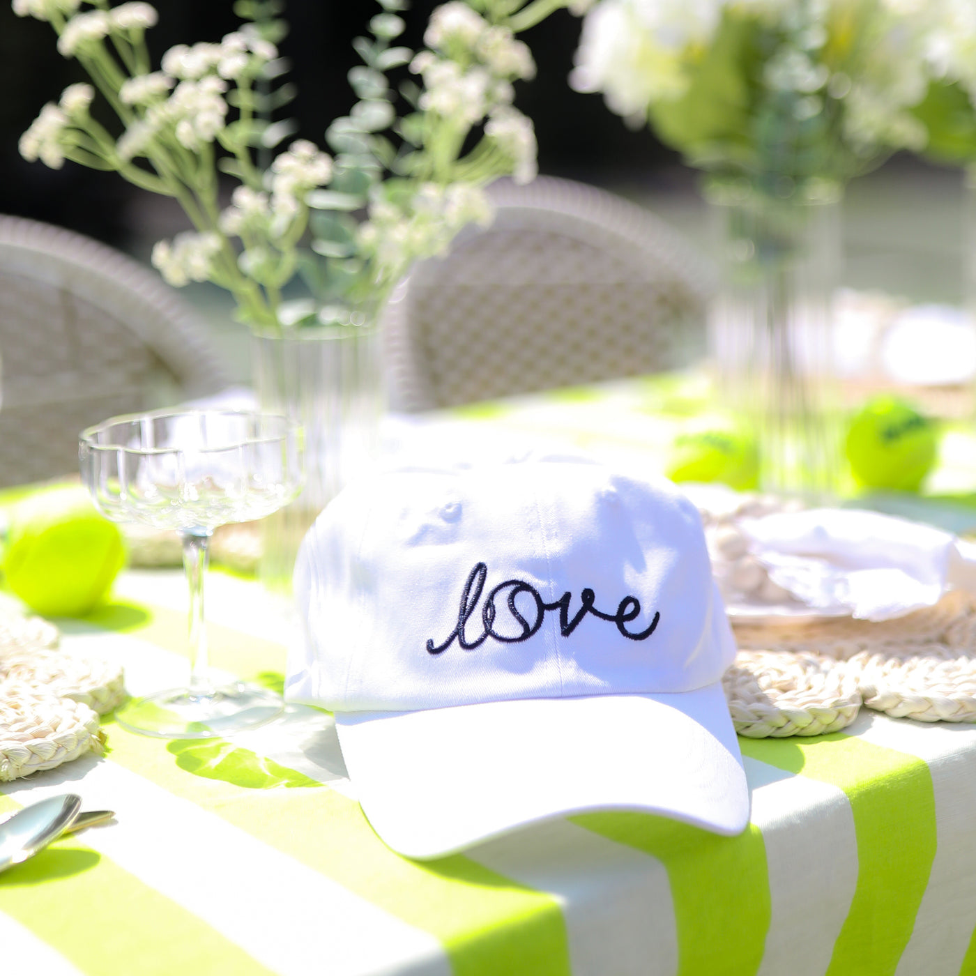 White hat sits on green and white striped tablecloth with the word love embroidered on the front in cursive