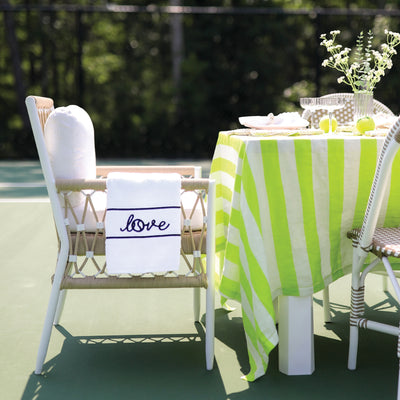 White terry towel laying over a chair arm with navy stripes and the word love embroidered on it. Towel is on a tennis court
