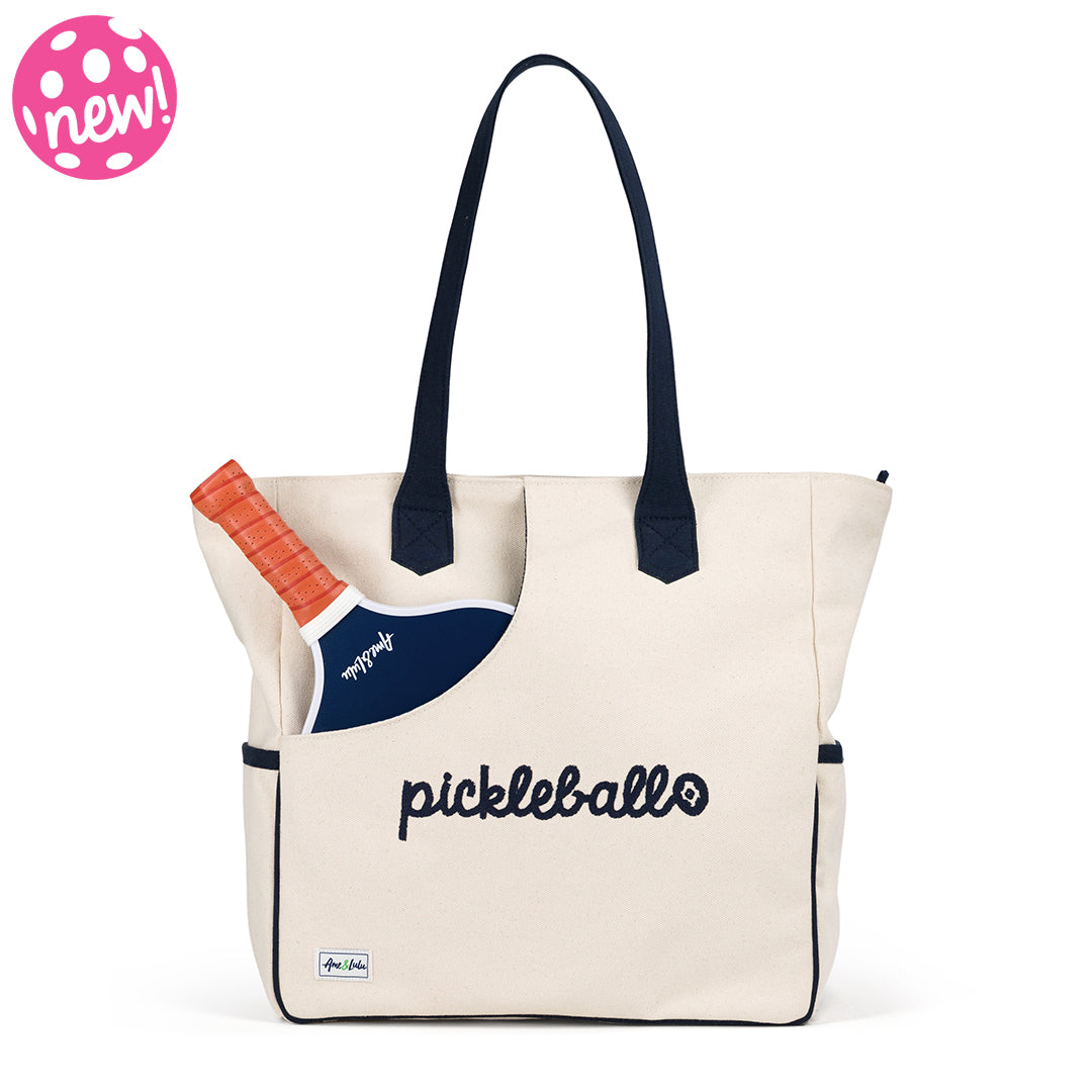Canvas tote with navy trim and navy handles. Front of tote has a slip pocket to hold pickleball paddles. Front is embroidered with the word pickleball in navy cursive font