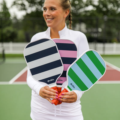 Model stands holding three paddles that are navy pink and blue