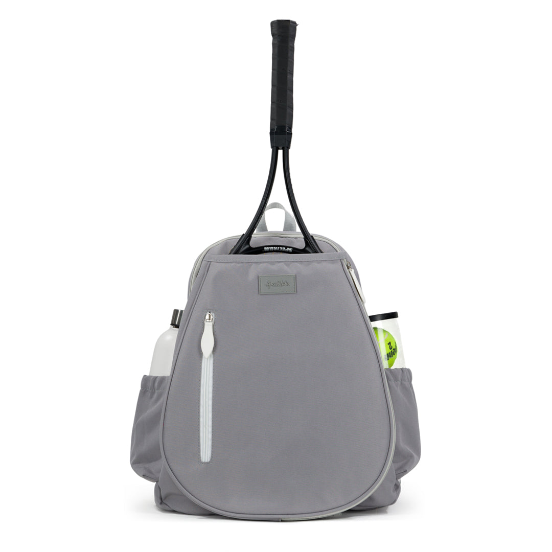 Front view of grey tennis backpack with white zipper on the front. There is a tennis racquet in the front pocket and a water bottle and tennis balls in the side pockets.