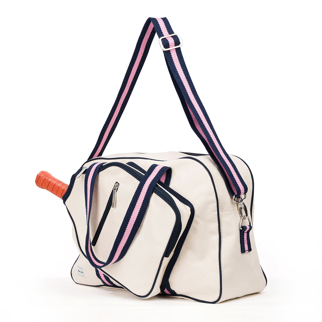 Side view of natural canvas pickleball tote with navy trim and navy and pink straps and handles.