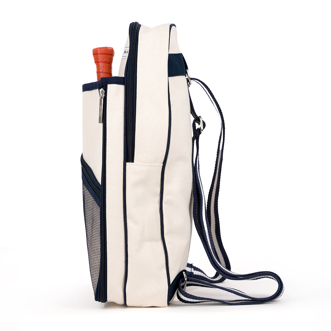 Side view of Hamptons pickleball sling bag. Bag has front mesh pocket and slip pocket on front to hold pickleball paddles. Bag has navy trim and navy and white striped straps. Bag has adjustable straps to be worn as a backpack or a crossbody.