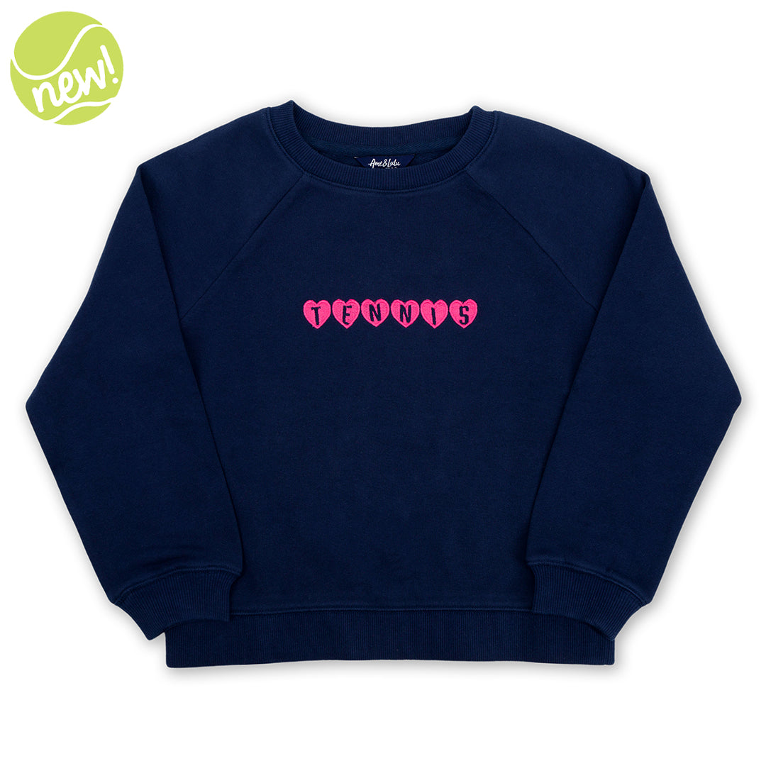 Navy kids sweatshirt lays flat on a white background. Pink hearts with the word tennis over them is embroidered on the front of the sweatshirt
