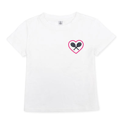 White kids t-shirt lays flat on a white background. There is a pink heart with navy crossed racquets inside embroidered on the pocket area of the shirt