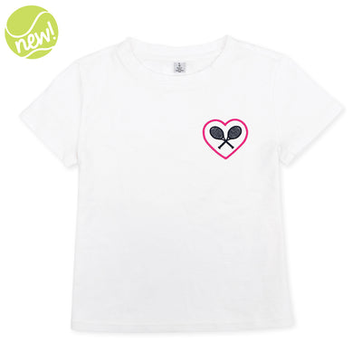 White kids t-shirt lays flat on a white background. There is a pink heart with navy crossed racquets inside embroidered on the pocket area of the shirt