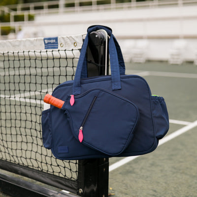 Front view of navy pickleball tote with hot pink zipper pulls. Tote has pickleball paddle shaped front pocket and side pockets for water bottles.