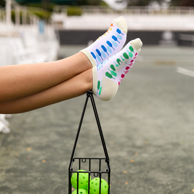 Pair of womens socks in white with light green trim and rainbow paddles stitched on it. Paddles are in the colors blue, green, pink and orange.