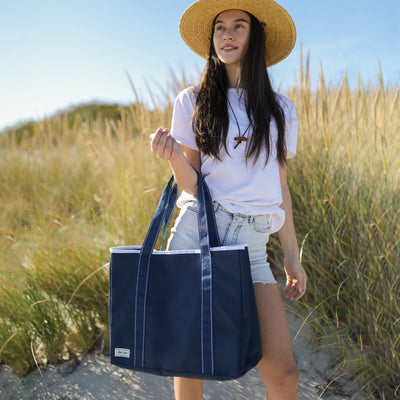 models stands on beach holding navy beach tote with navy straps and white details.