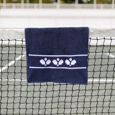 Navy cotton terry towel with three sets of white crossed paddles embroidered on the bottom of the towel