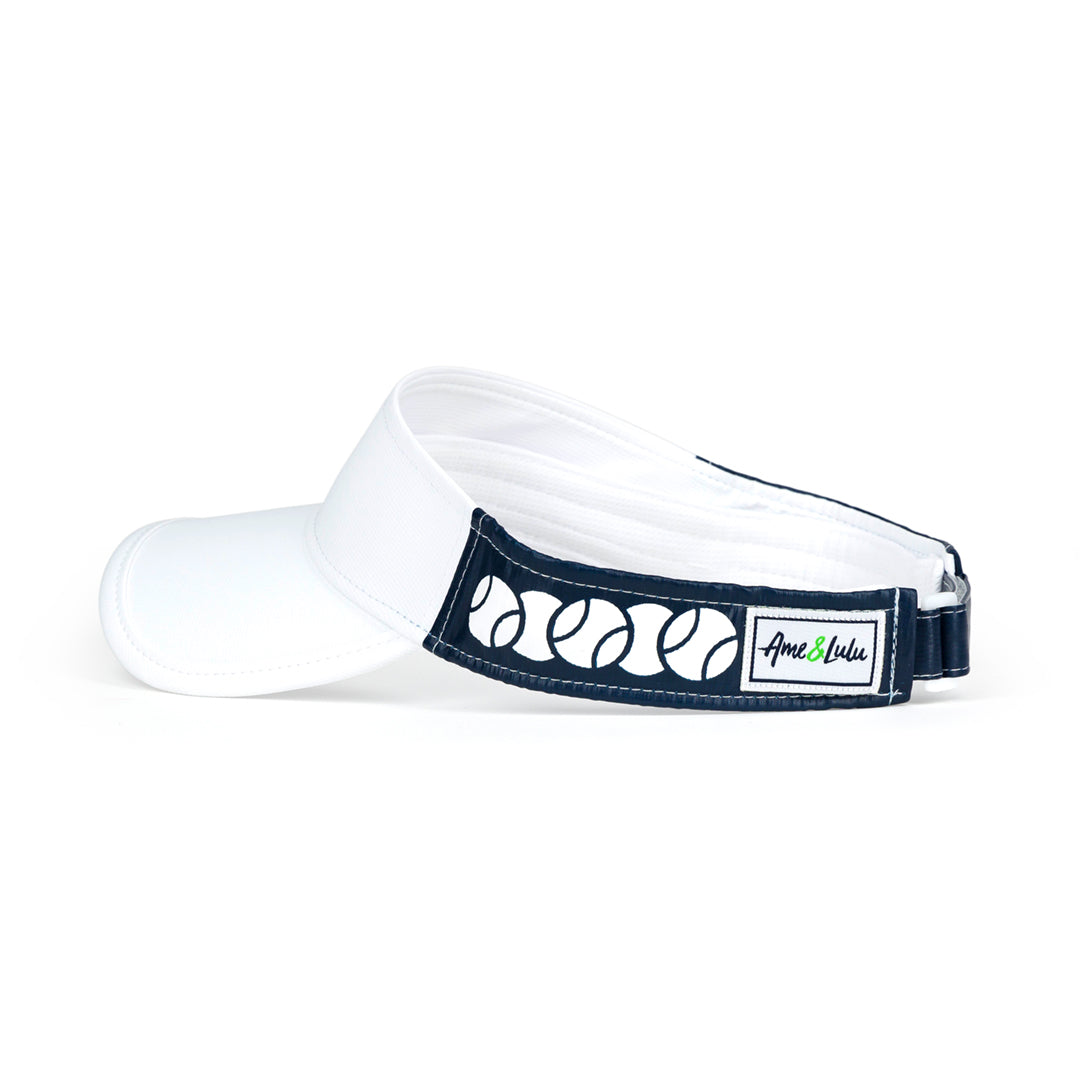 Side view of tennis ball overlap head in the game visor. Front of visor is white and sides are navy with white tennis balls printed on the sides.