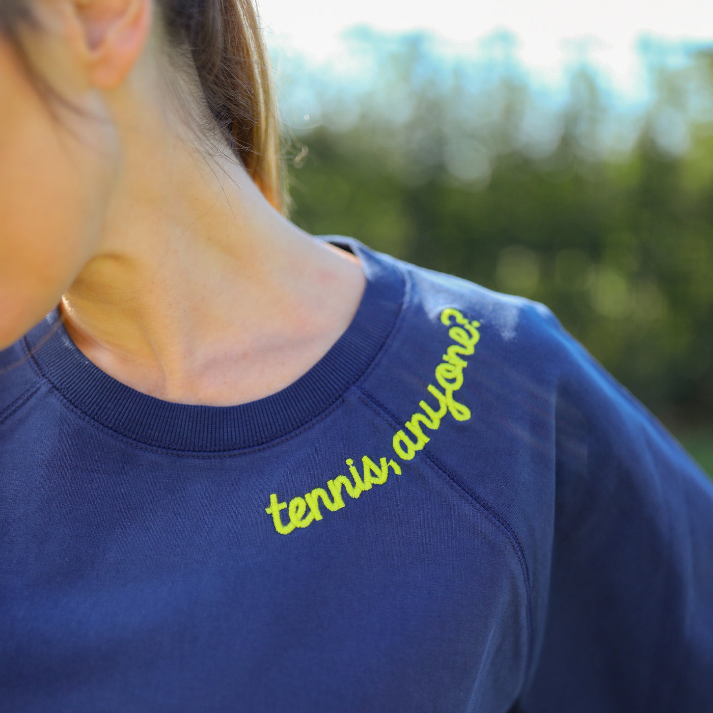 Navy women's sweatshirt with lime embroidery on neckline that reads "tennis anyone" and embroidered tennis ball patches on the elbows.