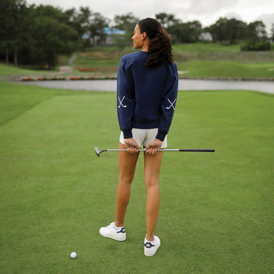 Navy womens cotton sweatshirt with "hold in one" in white cursive font embroidered on the neckline and white crossed golf clubs embroidered on the elbows.