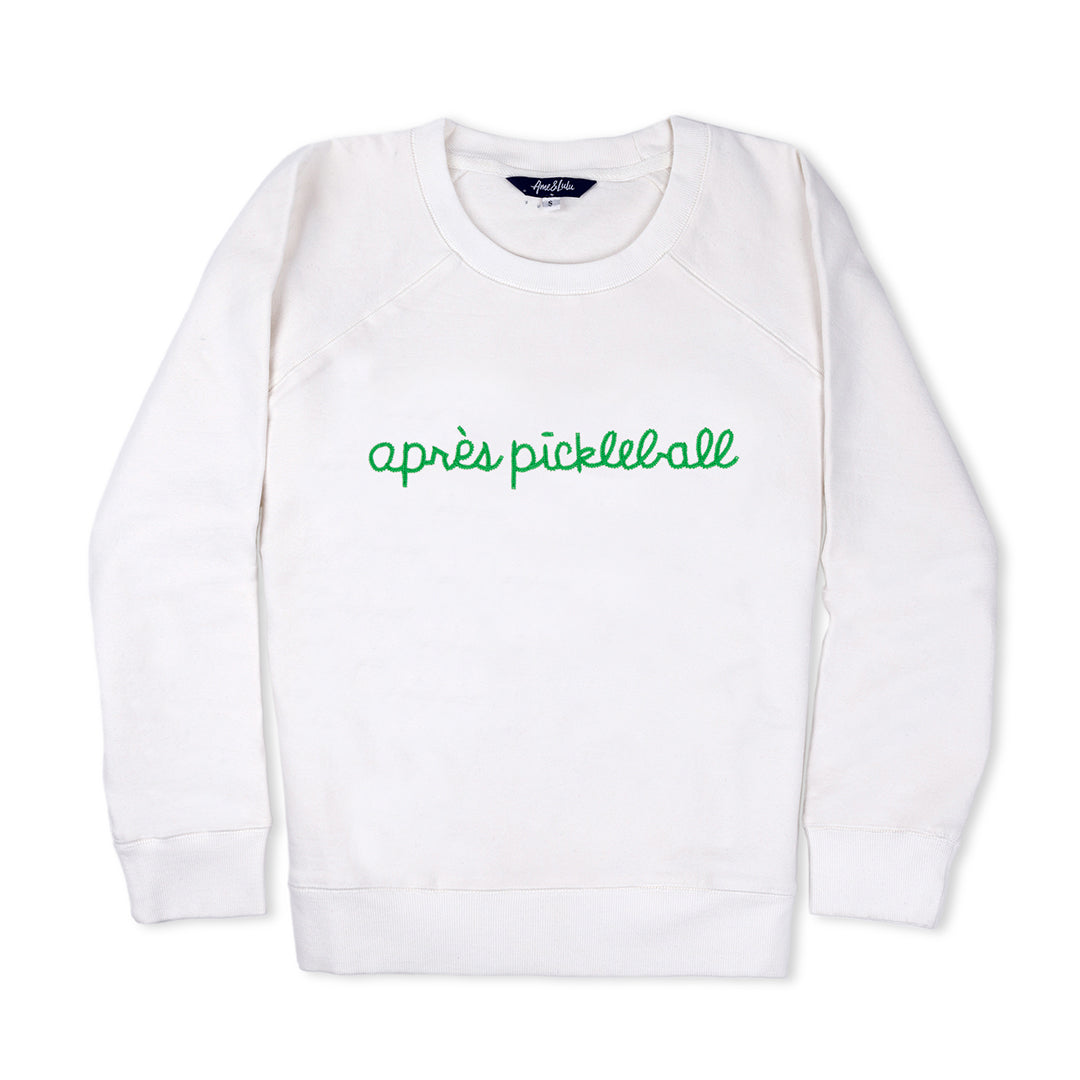 White sweatshirt lays flat on white background with green text reading apres pickleball embroidered on the front