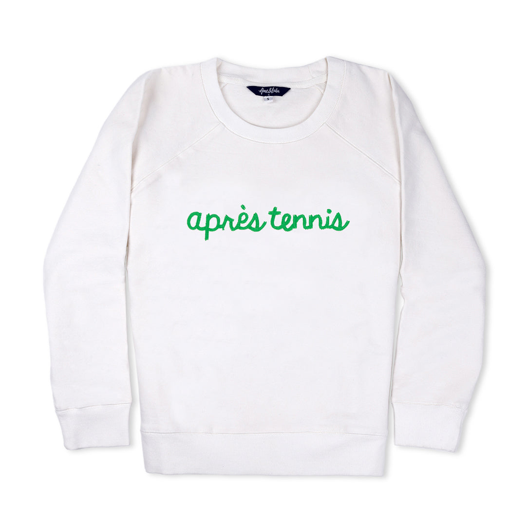 White sweatshirt lays flat on white background with green text reading apres tennis embroidered on the front