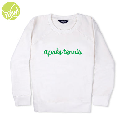 White sweatshirt lays flat on white background with green text reading apres tennis embroidered on the front