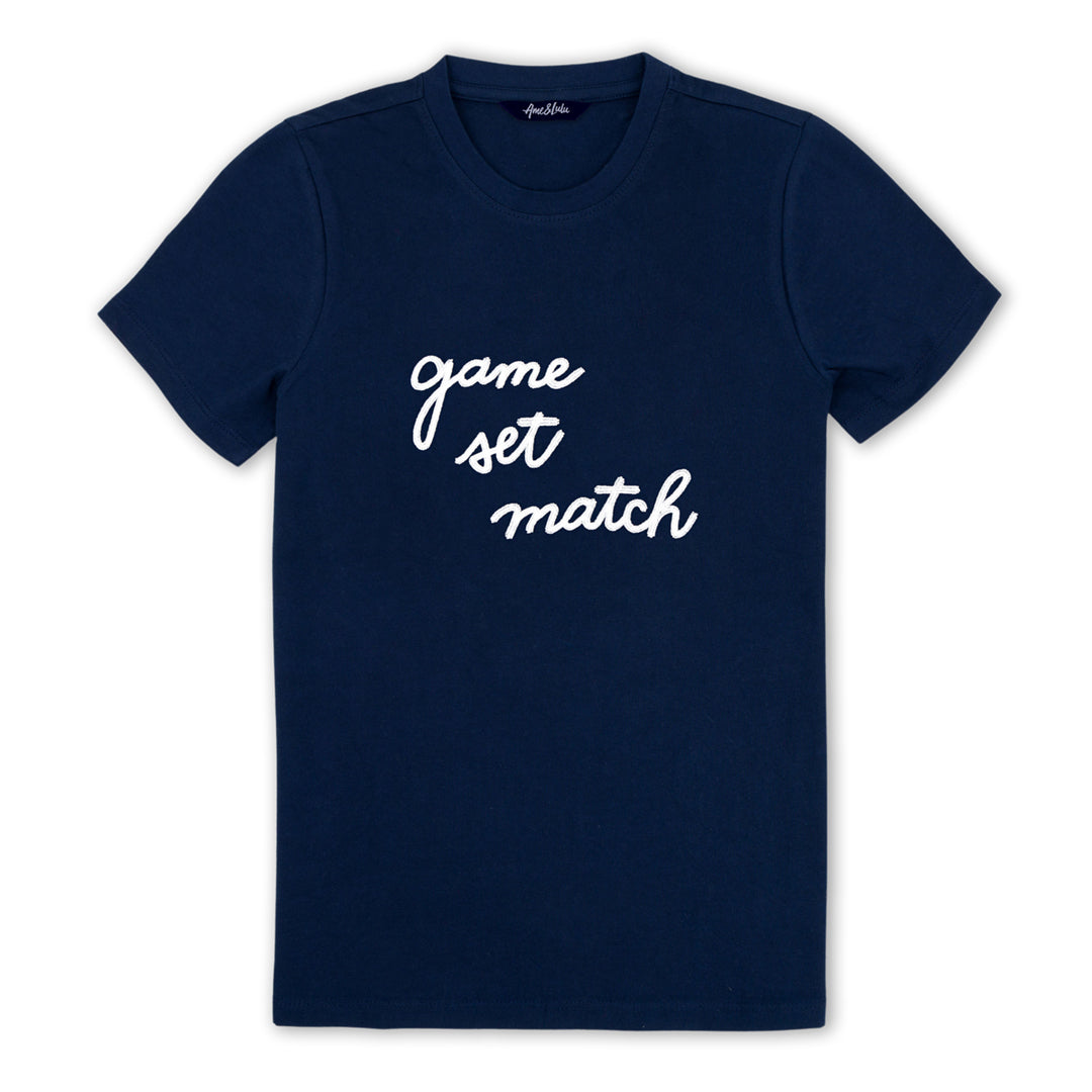 Navy t shirt lays flat on a white background with the words "game set match" embroidered on the front in white