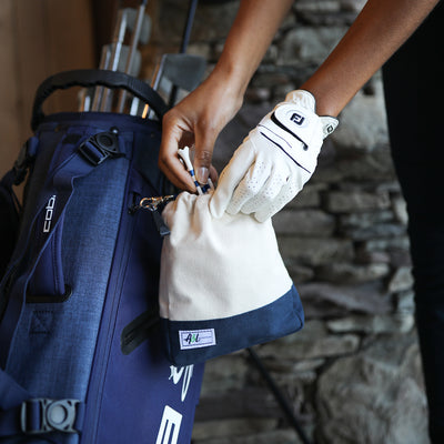 woman wearing golf glove holds tan canvas small drawstring pouch with navy trim.