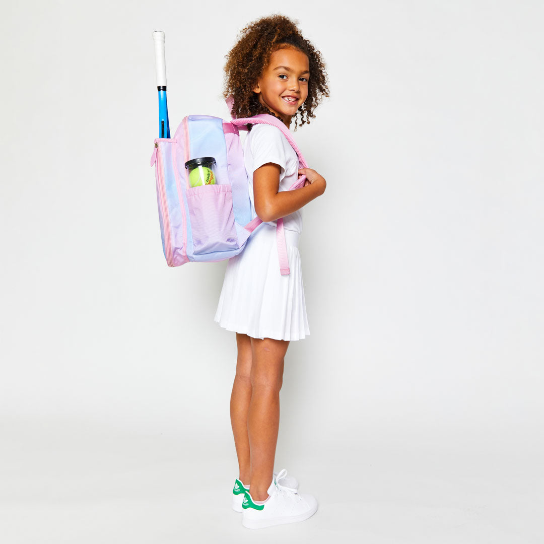 Little girl smiles wearing blue and pink ombre kids tennis backpack.