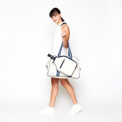 woman holding natural colored canvas pickleball bag on her arm with light blue and navy cotton webbing straps