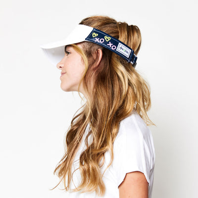 Little girl wearing navy kids visor with green heart shaped tennis balls and pink x and o printed on the sides.