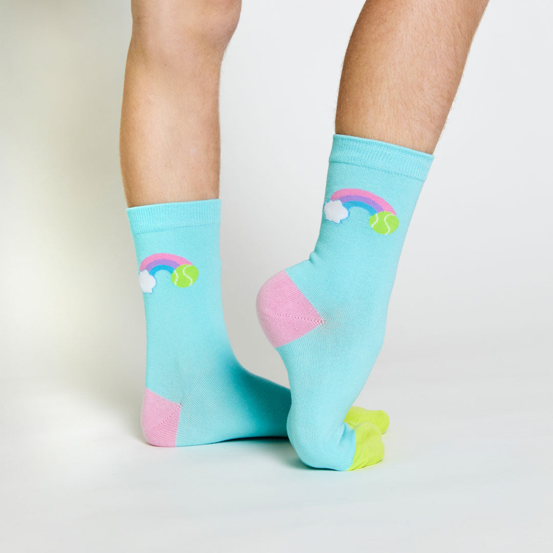 girl wearing pair of blue kids crew socks with pink and green heel and toes, with rainbow stitched on side of sock