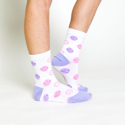 little girl wearing pair of white kids crew socks with purple and pink smiling tennis balls stitched all over socks
