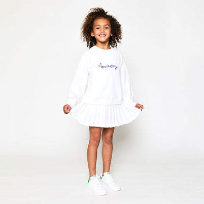 little girl wearing white kids sweatshirt with the word tennis star embroidered in purple cursive font on front and white tennis skirt