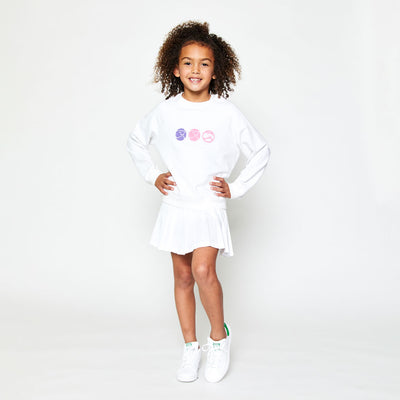 little girl wearing white kids sweatshirt with pink purple and white smiling tennis balls embroidered across the front