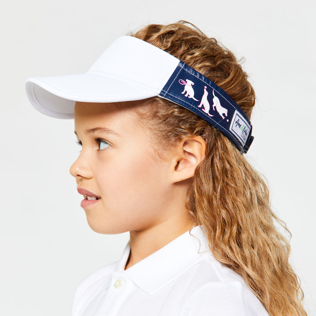 Little girl wearing navy kids visor with white and pink puppies playing tennis on the sides.