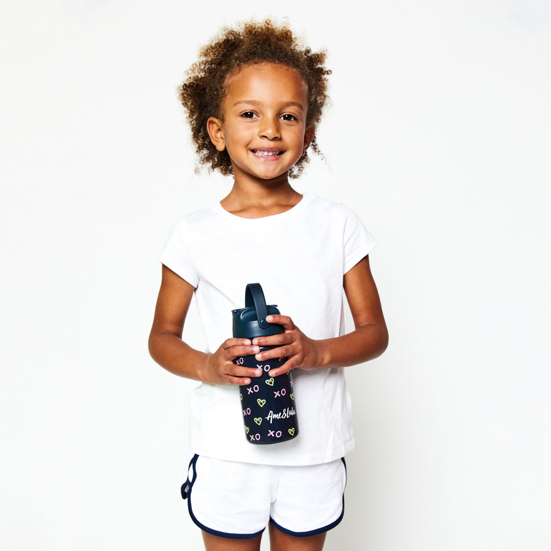 Little girl holding navy kids water bottle with green heart shaped tennis ball pattern