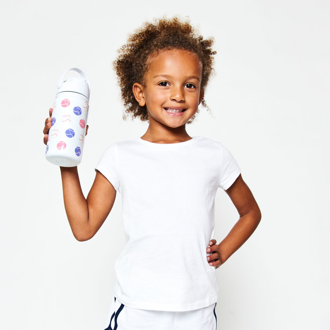 Little girl holding white kids water bottle with pink and purple smiling tennis ball pattern.