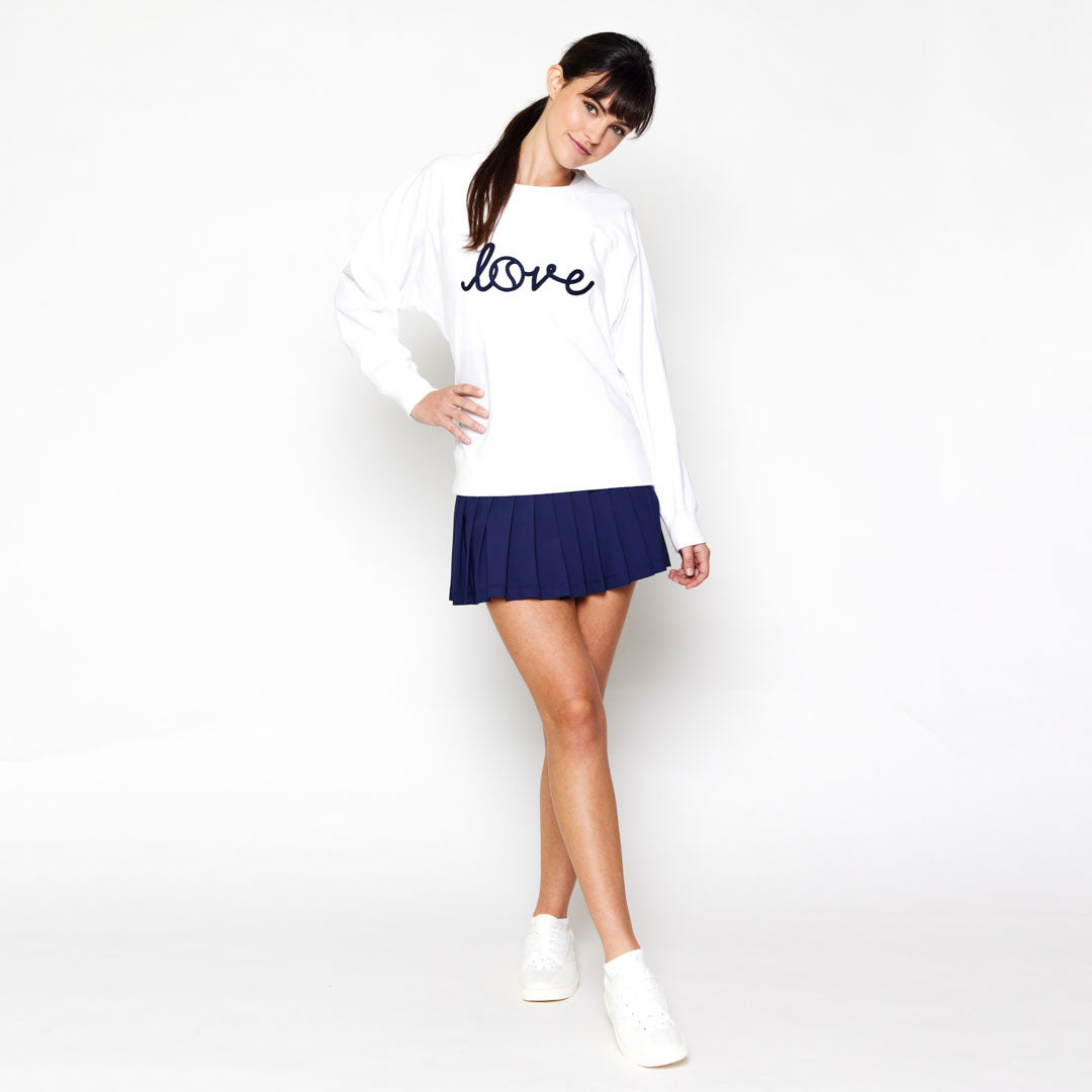 woman stands wearing white sweatshirt with the word love in cursive across front