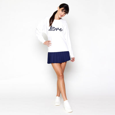 woman stands wearing white sweatshirt with the word love in cursive across front