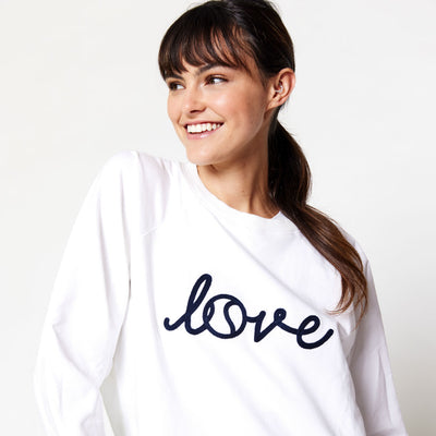 woman stands wearing white sweatshirt with the word love in cursive across front