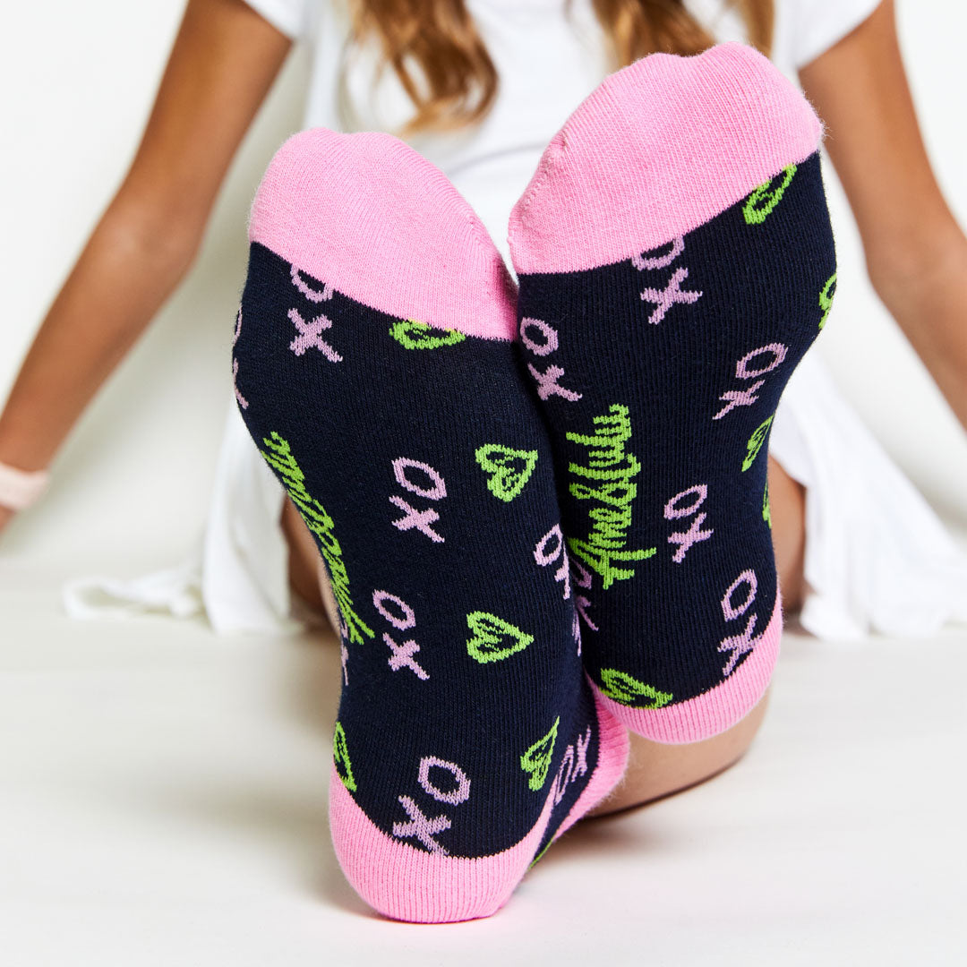 girl wearing pair of navy kids socks with pink heel and toes, and green heart shaped tennis balls