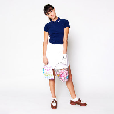 woman stands holding basket of golf balls and white small pouch with rainbow tie dye pattern and blue zippers