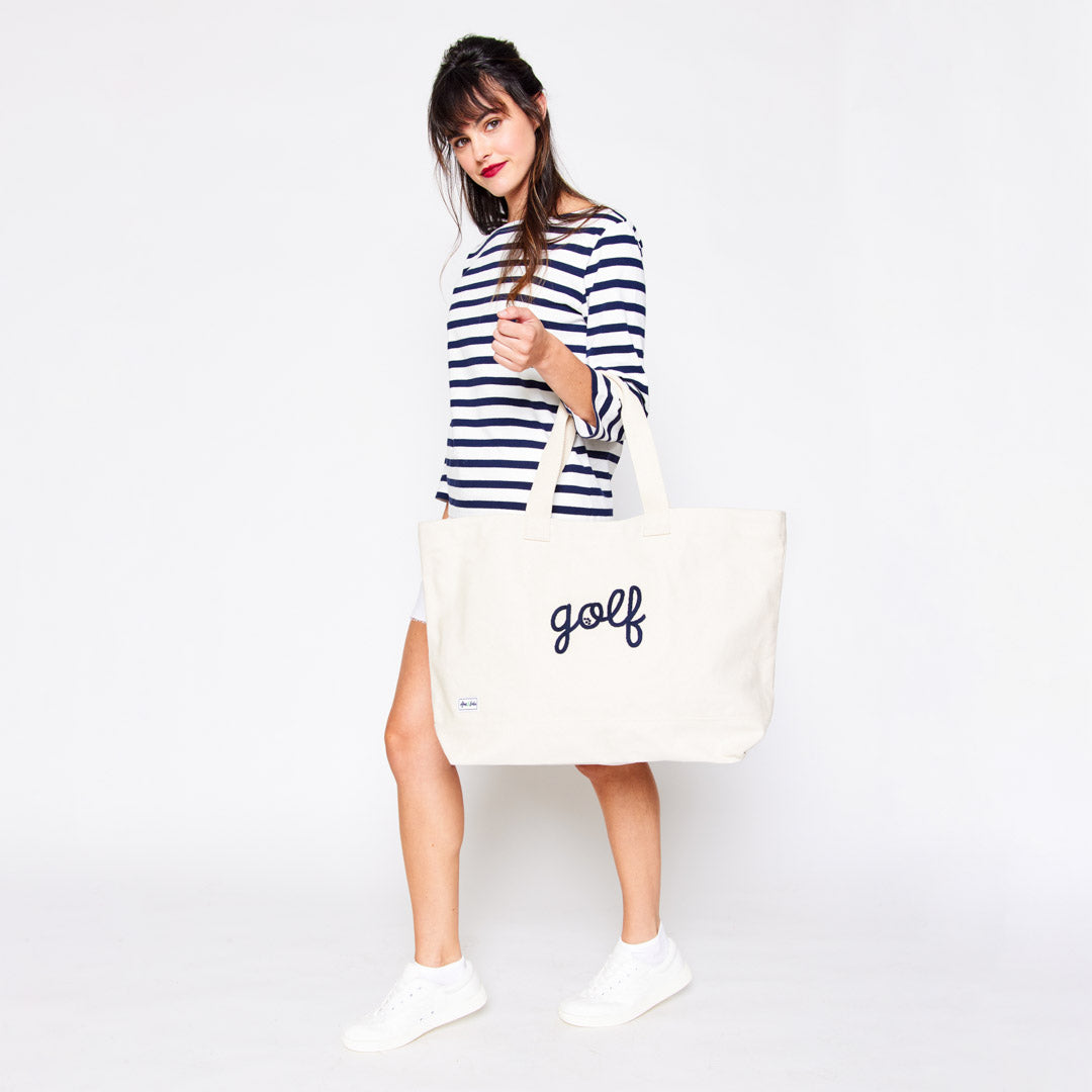 woman holding a canvas tote with the world "golf" stitched in navy cursive