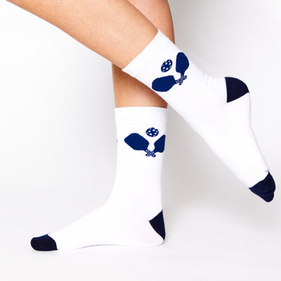 woman wearing white crew socks with navy toe and heel and crossed pickleball paddle design on the ankle of the sock