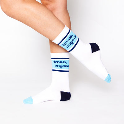 woman wears a pair of white socks with navy heel and blue toes. Navy and blue stripes wrap around ankle of sock with the text tennis anyone in cursive font