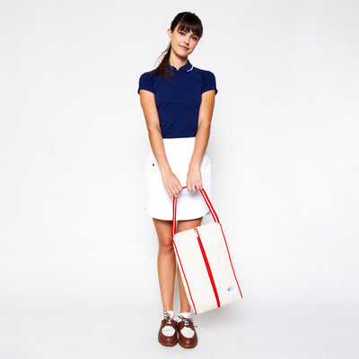 woman swings in front of her a rectangular tan canvas shoe bag with red handles.
