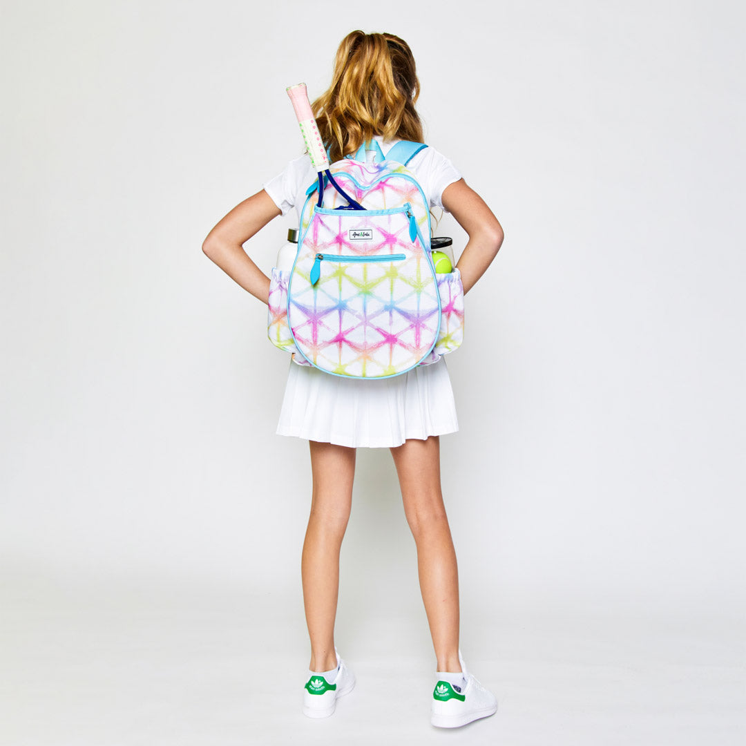 Girl stands wearing a white kids tennis backpack with rainbow shibori tie dye pattern.