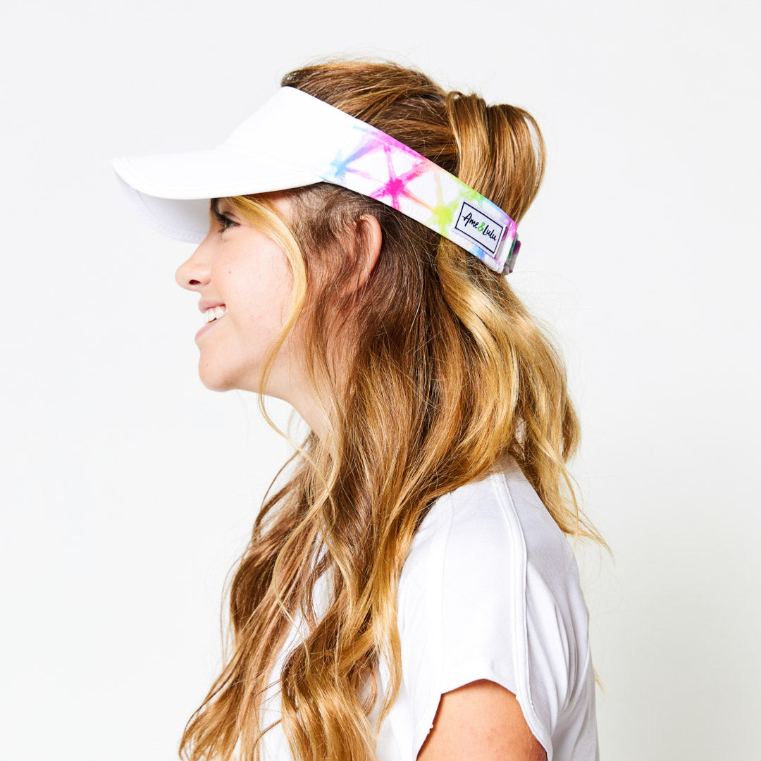 Little girl wearing white kids visor with rainbow tie dye pattern on the sides.